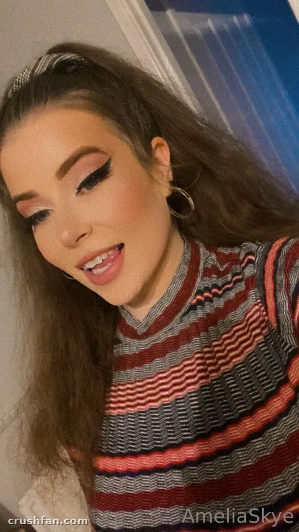 Amelia Skye tilting her head in a striped knit top and hoop earrings indoors