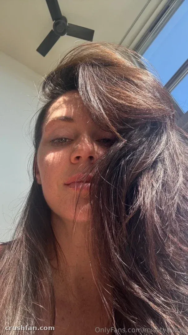 Alison Tyler taking a sunlit indoor selfie with loose dark hair across her face