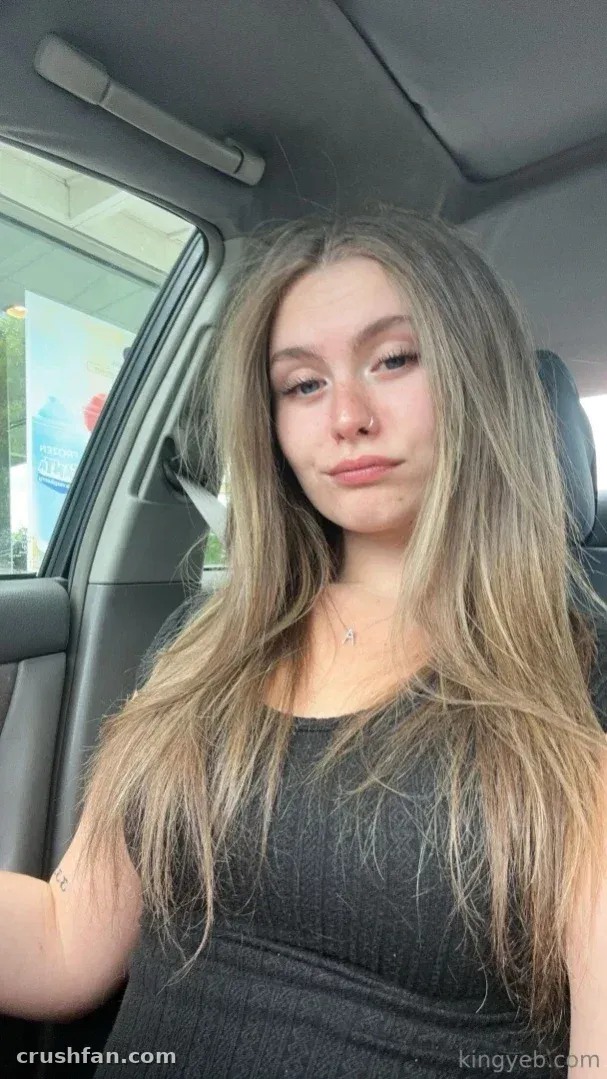KINGYEB™ en un coche, con una camiseta gris oscuro y el pelo largo y rubio.