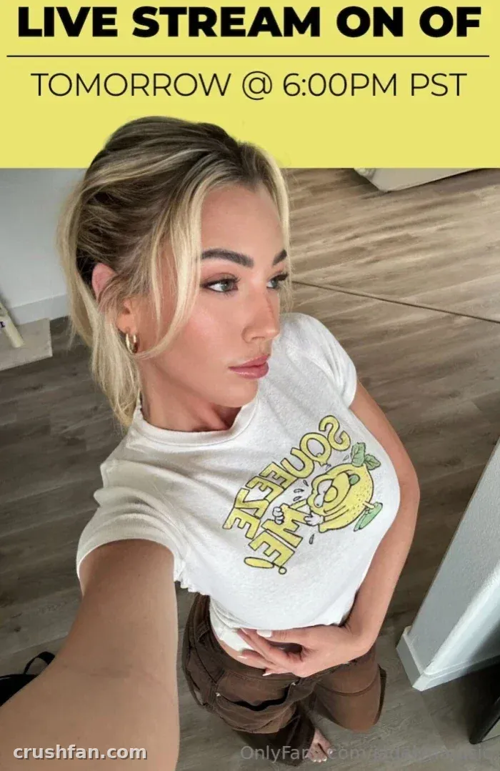Jadelyn in a white graphic tee and brown trousers taking an indoor selfie with a live stream announcement banner