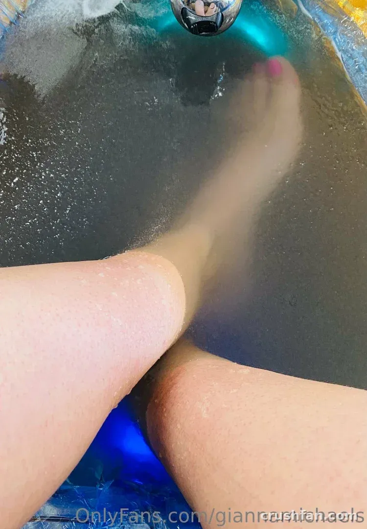 Pernas de uma mulher descansando em uma jacuzzi borbulhante com água iluminada em azul e unhas dos pés rosadas