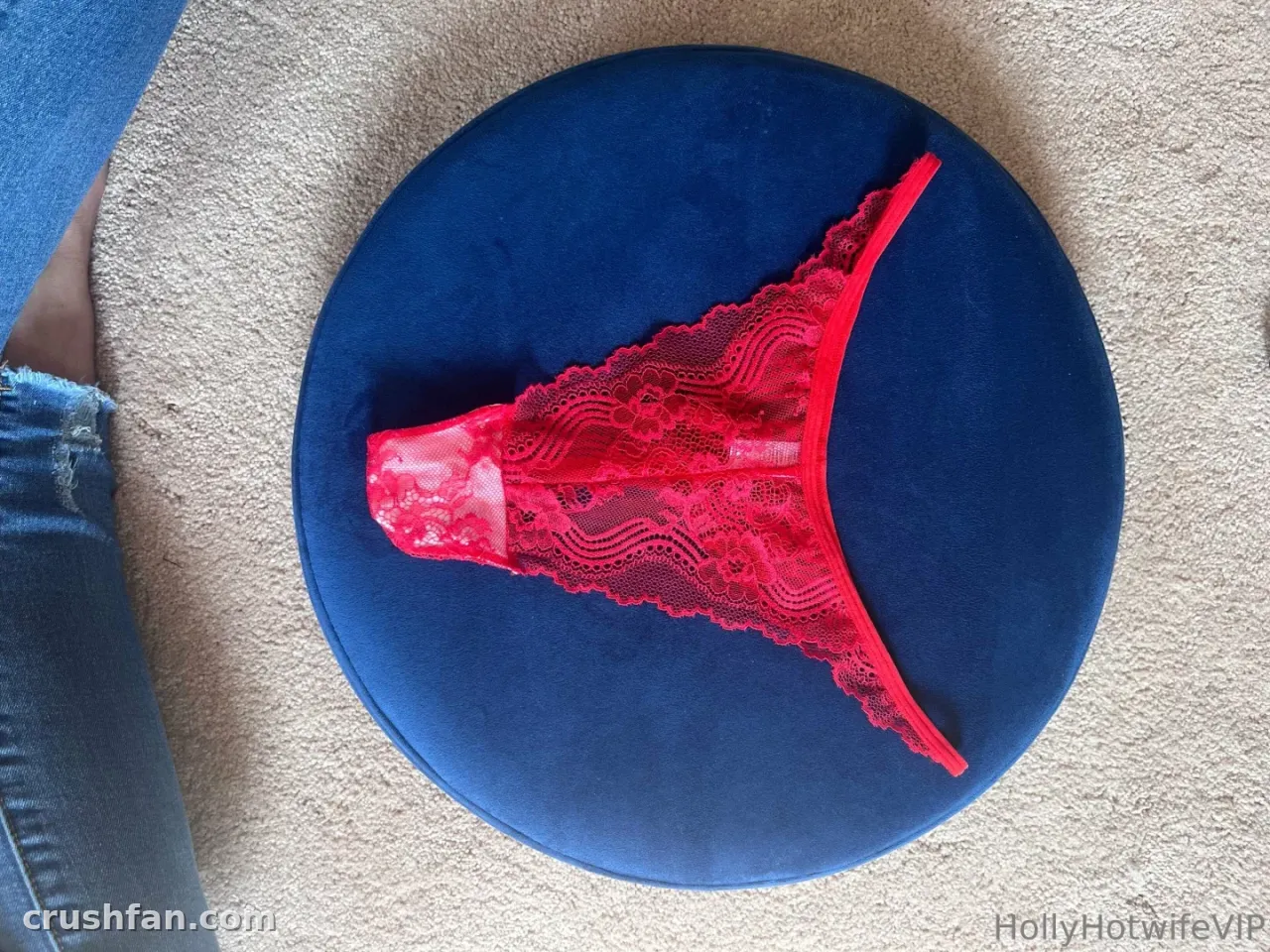 String en dentelle rouge sur un tabouret rond en velours bleu à côté d'un denim bleu sur une moquette beige