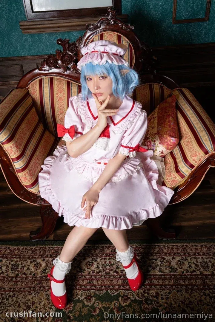 Creator in a pink maid dress with red bows seated on a vintage chair indoors