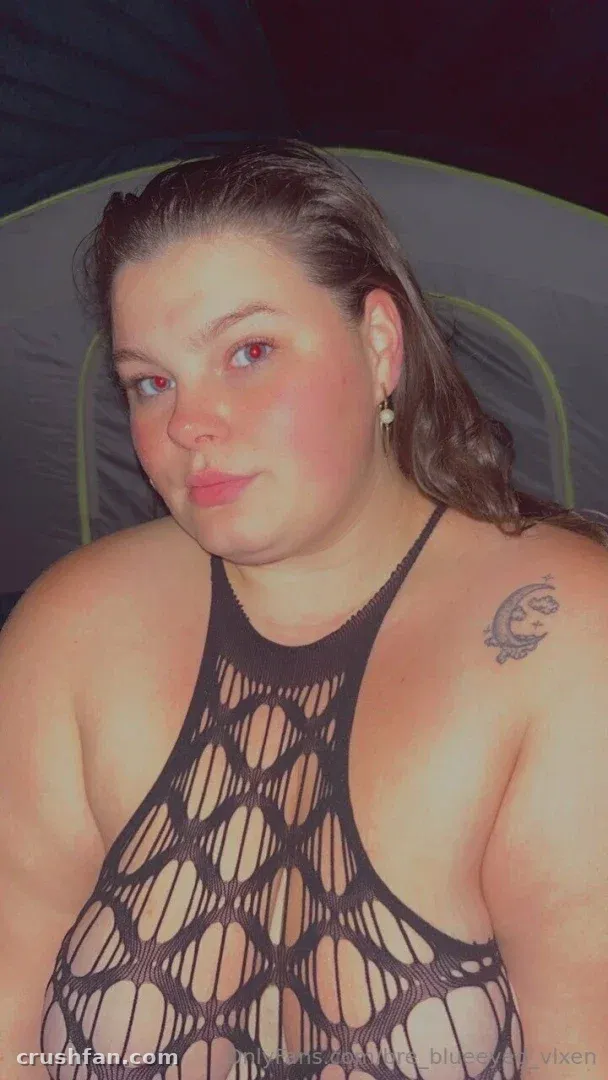 Miss Bunny in a black net top inside a tent, looking at the camera.