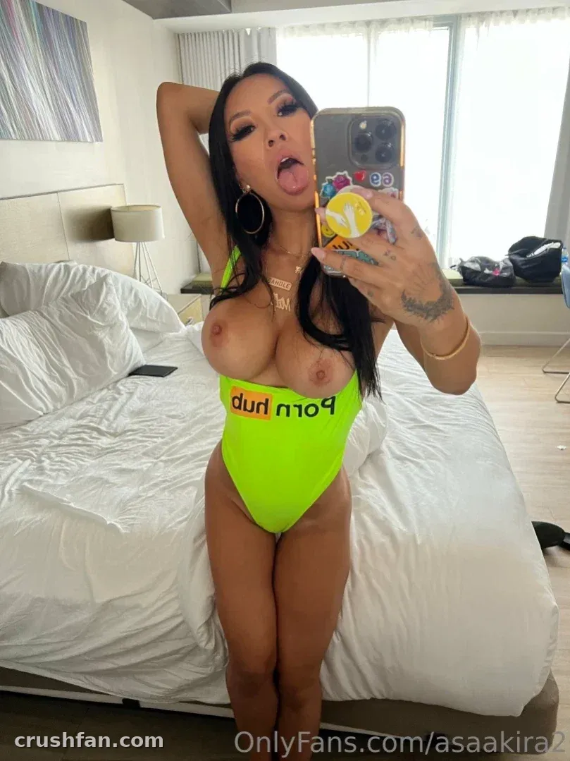 Asa Akira in einem neongrünen Bodysuit beim Spiegel-Selfie in einem hellen Schlafzimmer