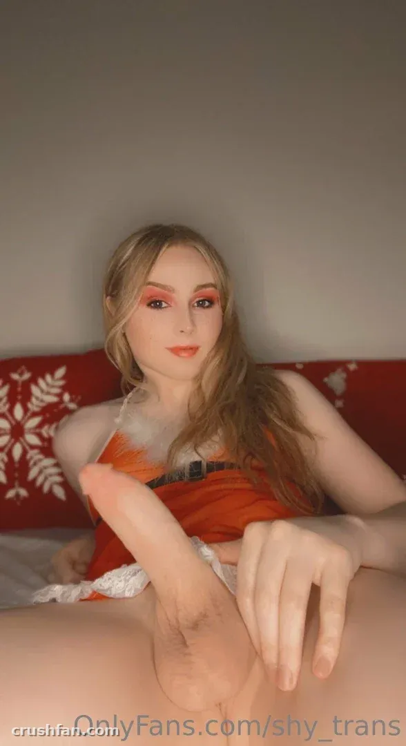 Sarah com um top laranja apoiada em uma almofada vermelha de flocos de neve sob uma suave luz interna.