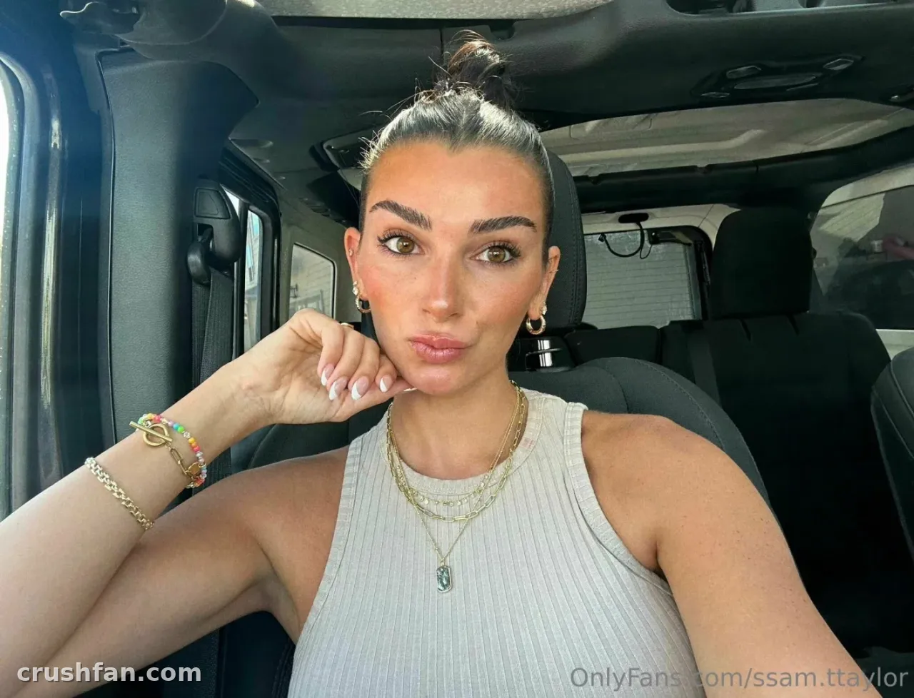 Sam Taylor in a light ribbed top inside a car, wearing layered gold jewellery.