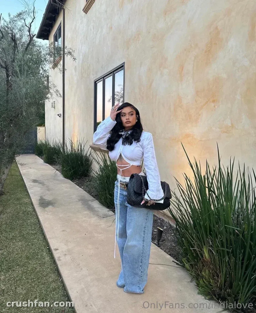 India Love com um top branco e calça jeans de perna larga em pé em uma passarela ao ar livre