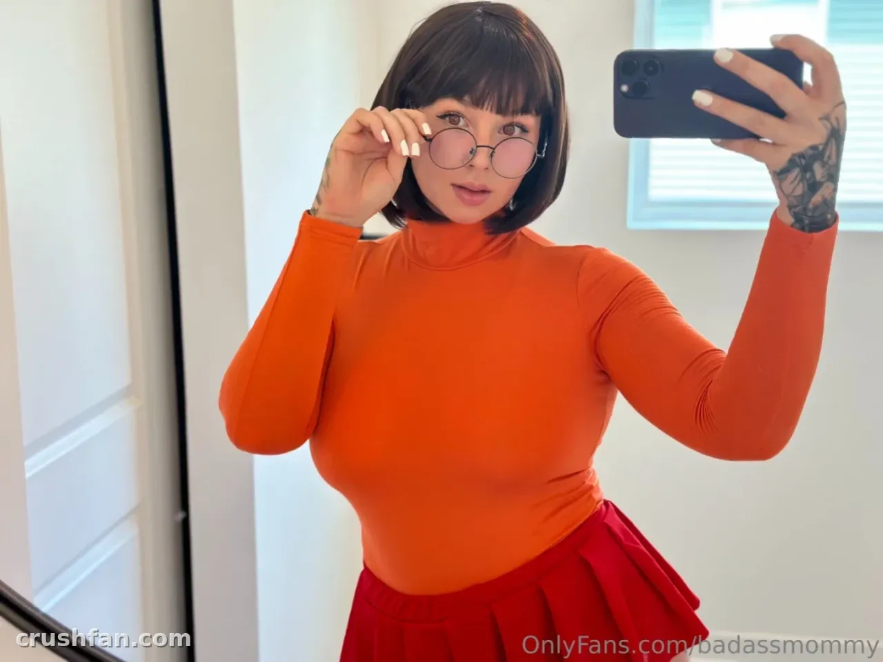 Sara in einem orangefarbenen Top und rotem Rock, die beim Halten einer Brille ein Spiegel-Selfie macht