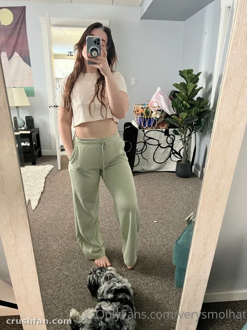 Smol tira uma selfie no espelho com uma camiseta cropped e calça jogger verde-sálvia em um quarto com carpete.