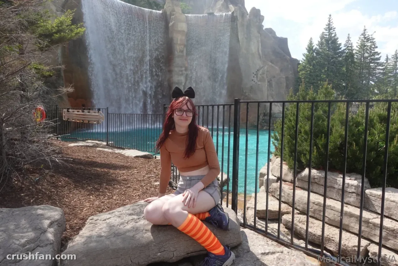 Creator in a rust top and striped socks sitting on a rock before a waterfall
