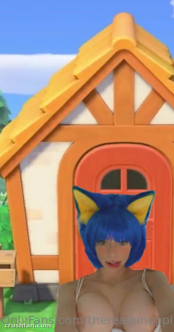 PinupPixie com peruca chanel azul e orelhas de animal em frente a uma casinha colorida de estilo desenho animado