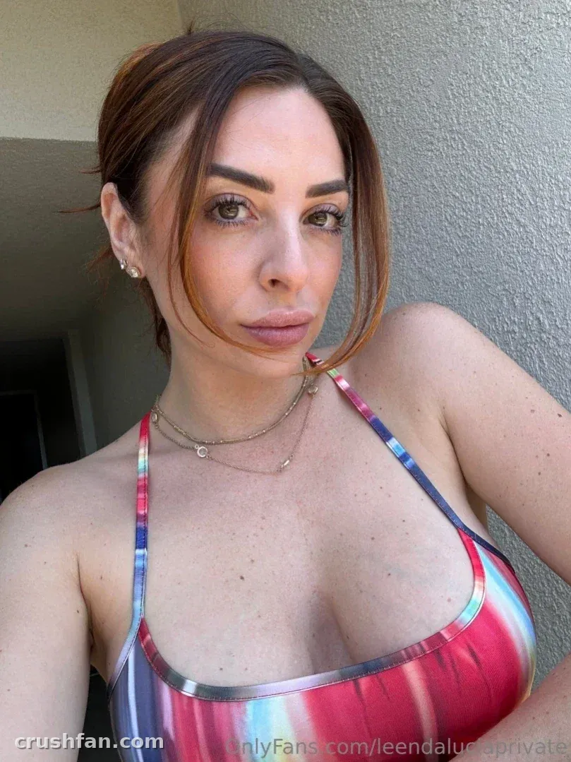 Leenda Lucia con un top halter metálico a rayas posando contra una pared gris a la luz del día