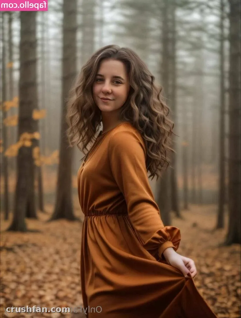 Leyla com um vestido laranja ferrugem em pé em uma floresta outonal enevoada com folhas caídas