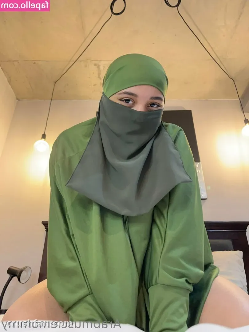 Criadora com lenço verde na cabeça e top combinando, rosto parcialmente coberto, em um ambiente com iluminação quente.