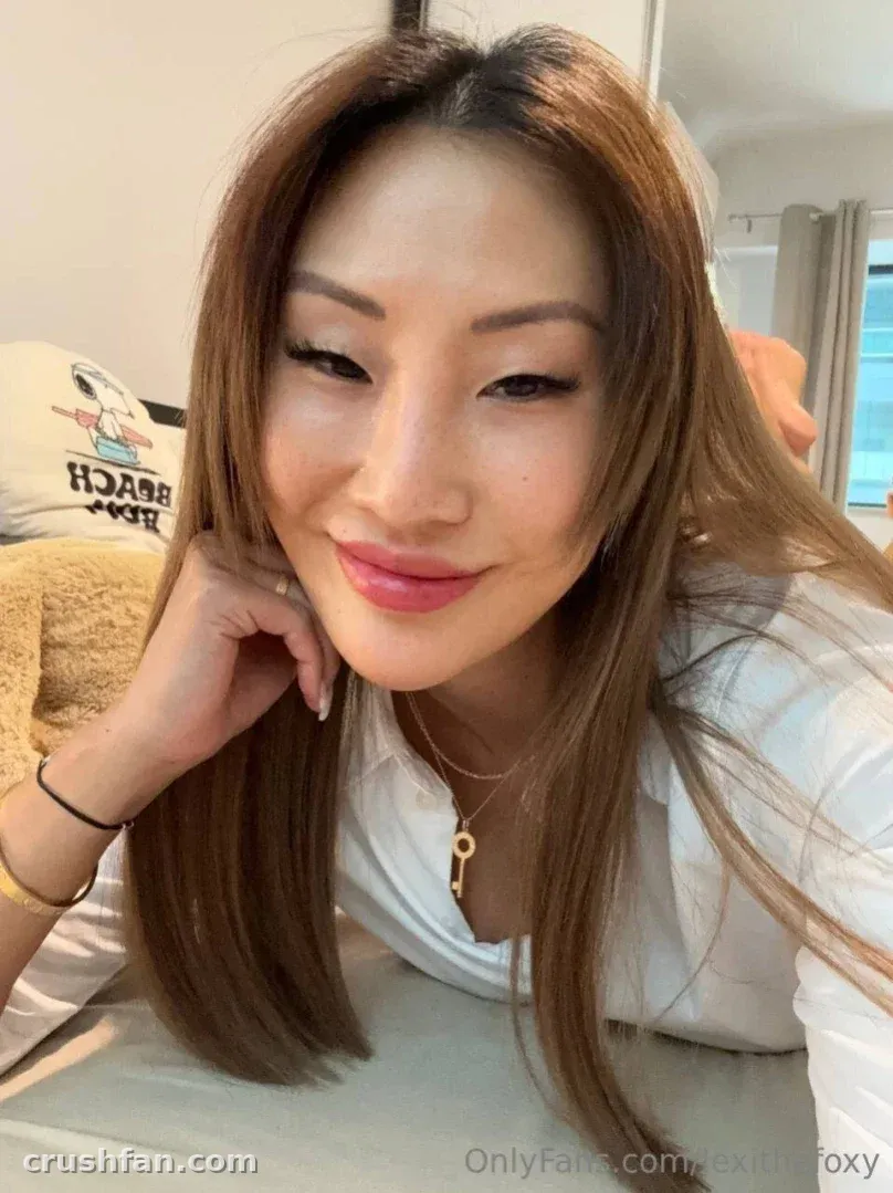 Lexi sonriendo en una selfie luminosa en interiores con cabello largo y una blusa blanca