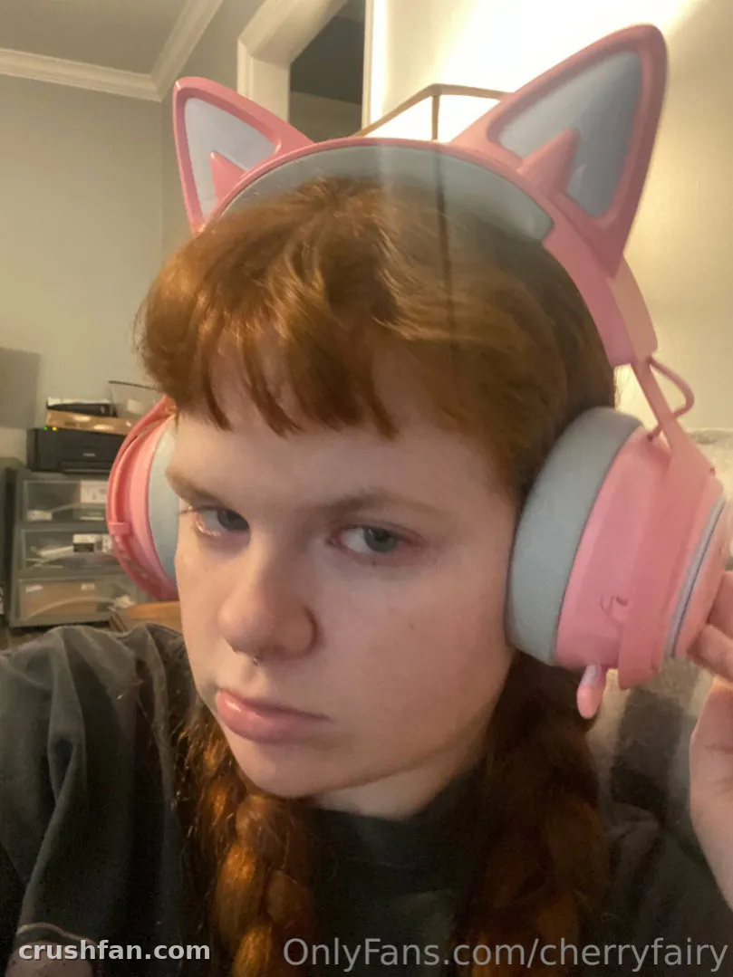 A criadora Cherry com fones de ouvido rosa com orelhas de gato, selfie em ambiente interno com expressão calma
