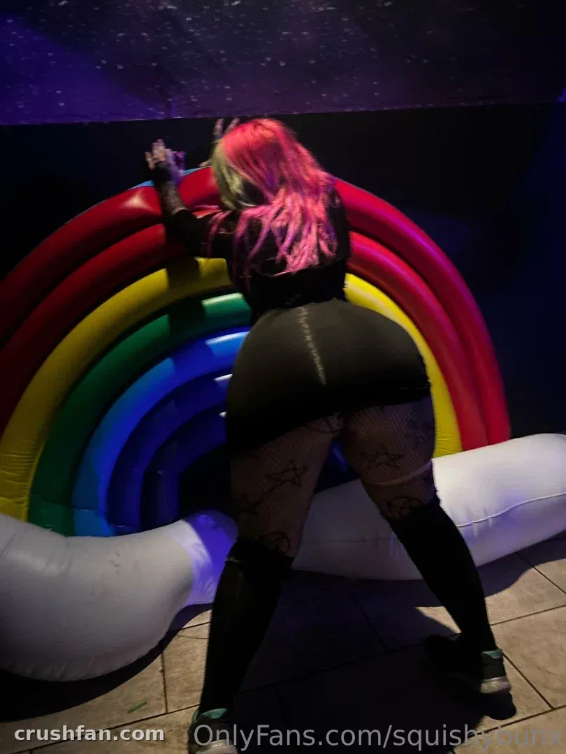 Brooke Ivy standing beside a glowing rainbow arch in a dark room