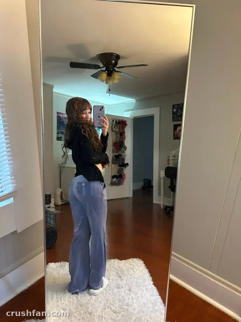Kali takes a mirror selfie in a black top and blue jeans, standing on a white rug indoors.