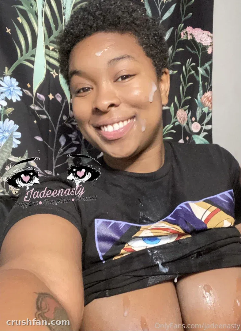 Creator in a black graphic t-shirt smiling in front of a dark floral wall covering