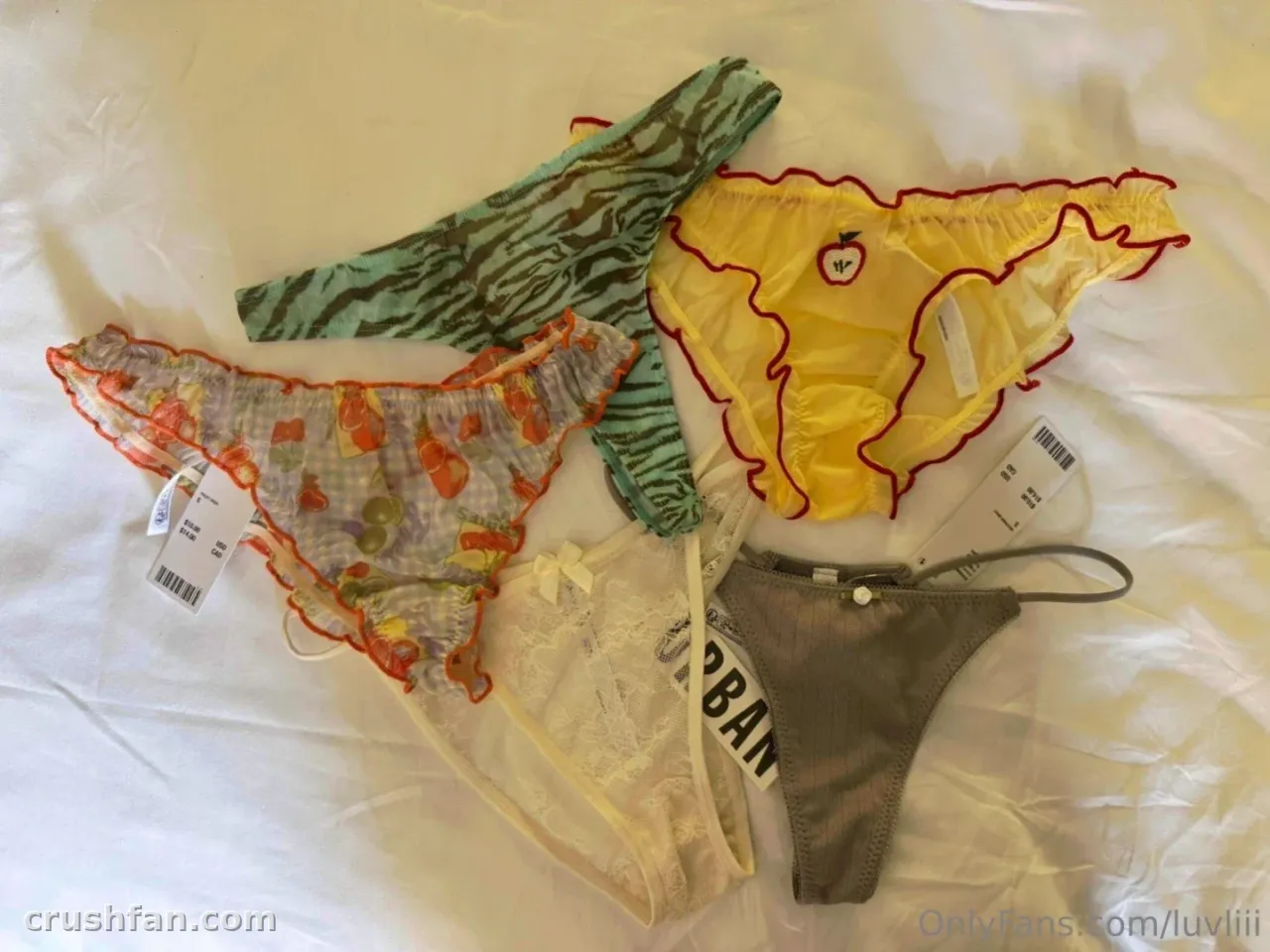 Composición plana de ropa interior colorida sobre ropa de cama blanca, incluyendo estampado de cebra, amarillo, blanco transparente y gris.