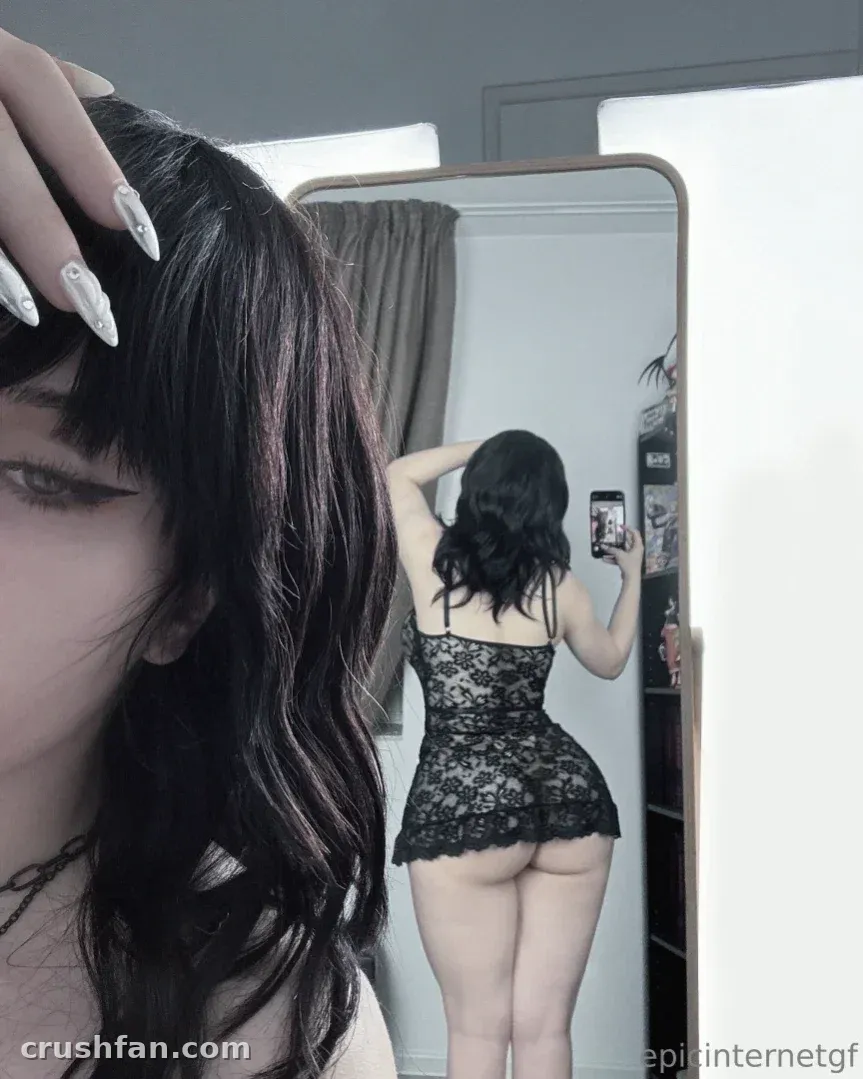 Anna in a black lace bodysuit taking a mirror selfie with long white nails visible.
