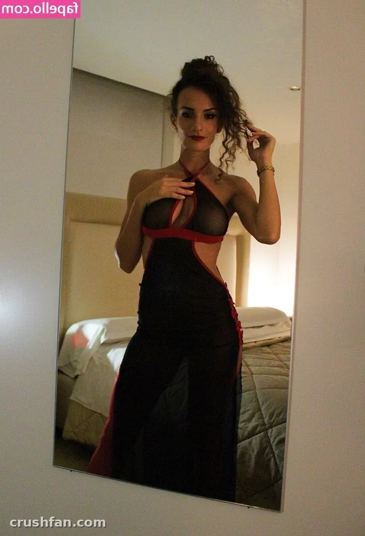 Woman in a black and red sheer gown posing in front of a mirror in a softly lit room