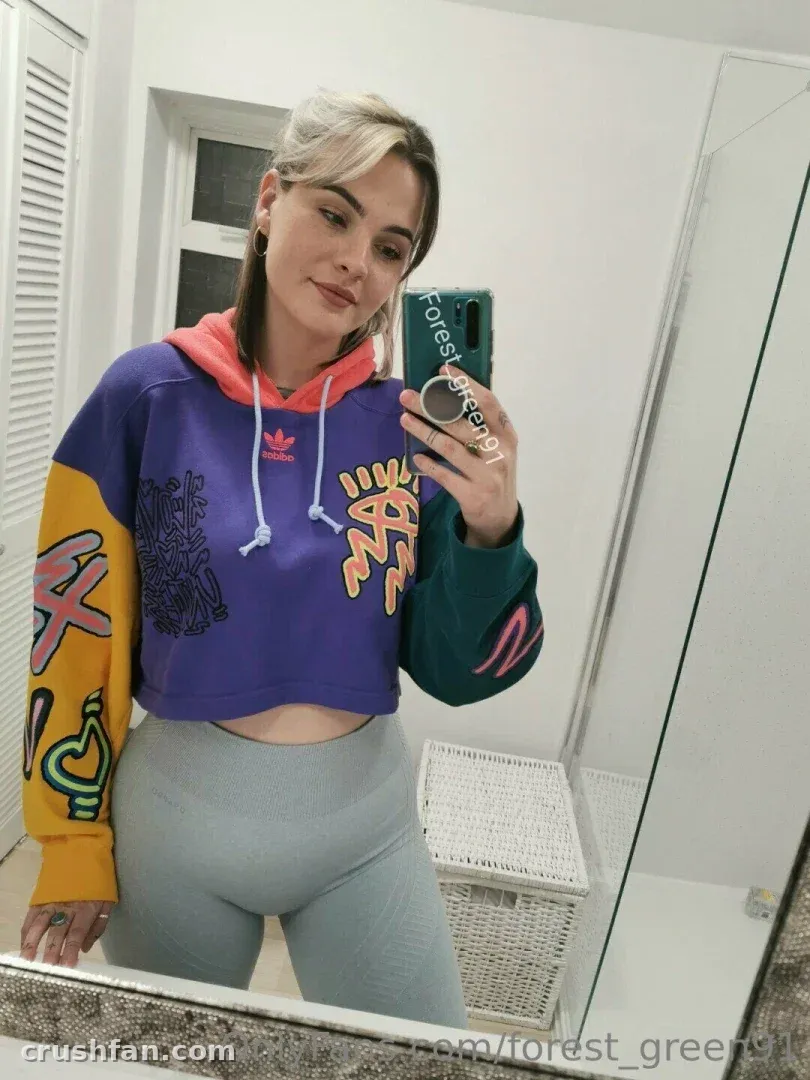 Forest Green com um moletom cropped color block e legging cinza tirando uma selfie no espelho