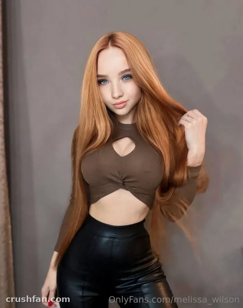 Melissa com um top marrom com recortes e calça de couro preta contra uma parede cinza