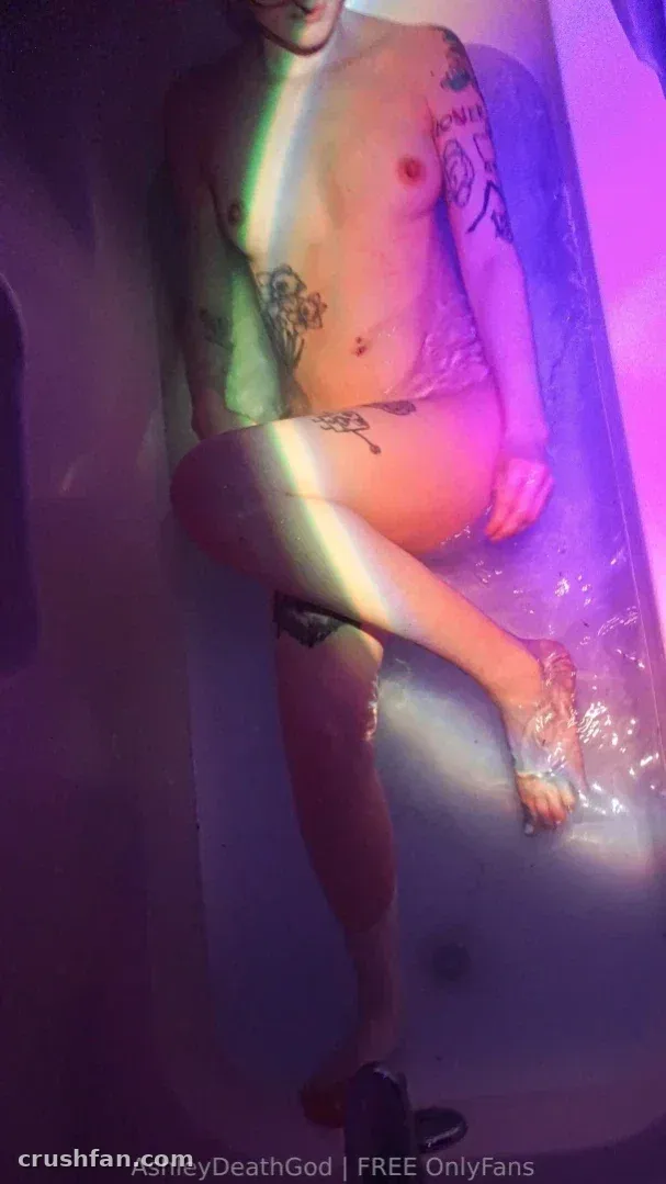 Ashley reclining in a bathtub with colourful neon lighting and plastic sheeting