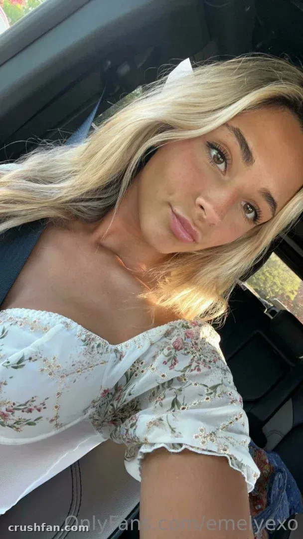 Em macht ein sonniges Selfie in einem Auto und trägt ein weißes Blumentop.