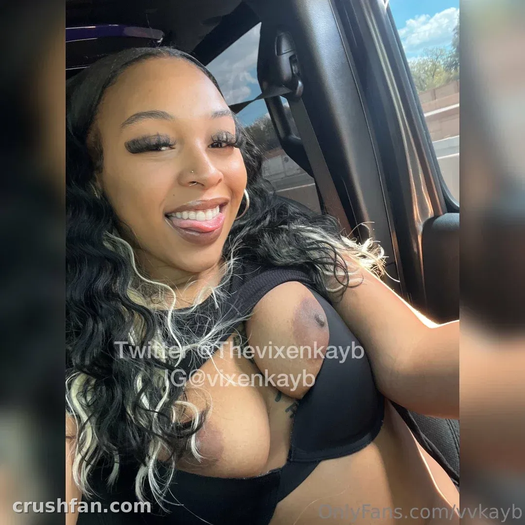 Virtual vixen smiling in a car selfie with long dark wavy hair and a black top