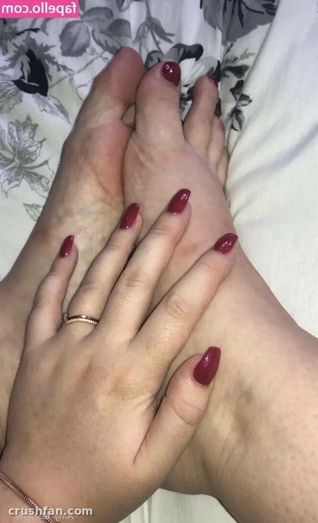 Close-up of hands with deep red nail polish resting on feet over floral fabric