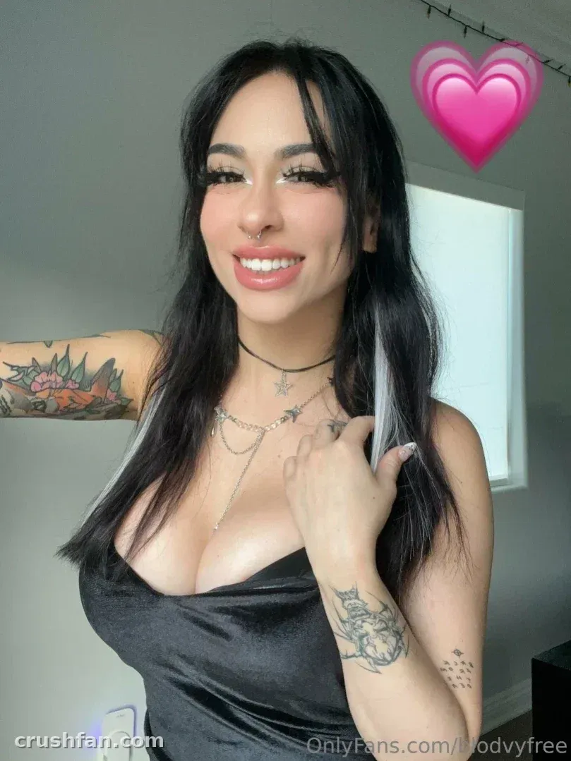 Femme souriante aux longs cheveux foncés, avec un haut noir et des tatouages en intérieur