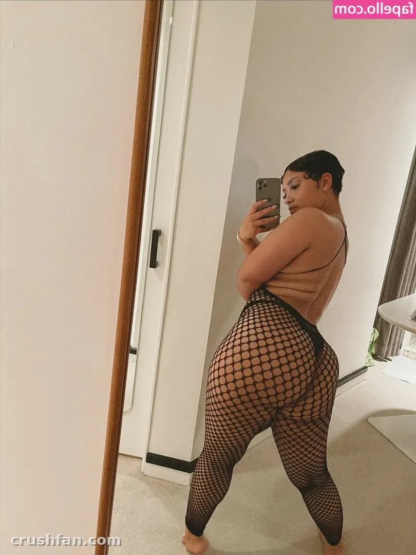 Creator in einem hellbraunen Oberteil und schwarzen Netzleggings, die in einem hellen Raum ein Spiegel-Selfie macht