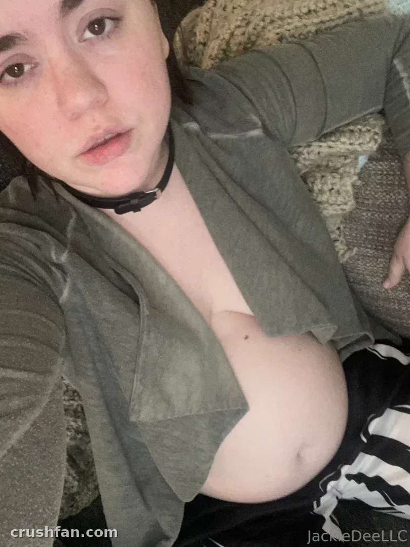 Jackie in einem olivfarbenen Top und schwarzem Choker, die drinnen an einer Strickdecke lehnt
