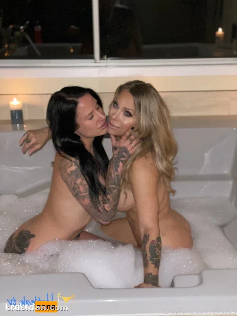 Duas mulheres com tatuagens sentadas juntas em uma banheira cheia de espuma à luz de velas