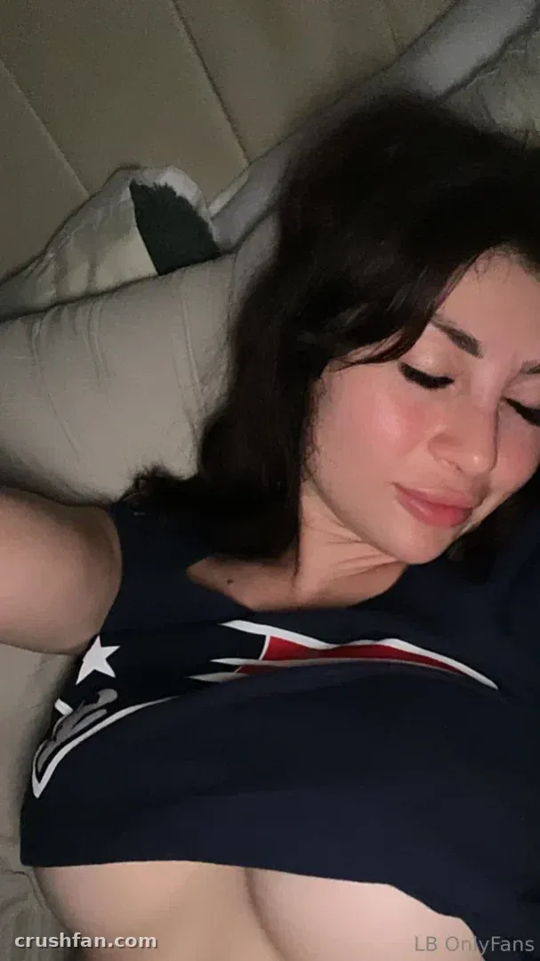 Lakette Barraza in einem dunkelblauen Sporttop, auf einem Bett mit heller Bettwäsche ruhend.