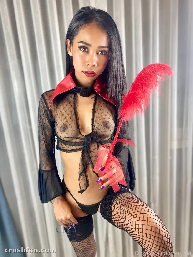 Ae Asia in sheer black lingerie with a red collar holding a red feather against draped curtains