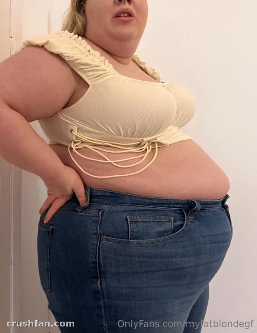Creator in a cream crop top and blue jeans standing against a white wall.