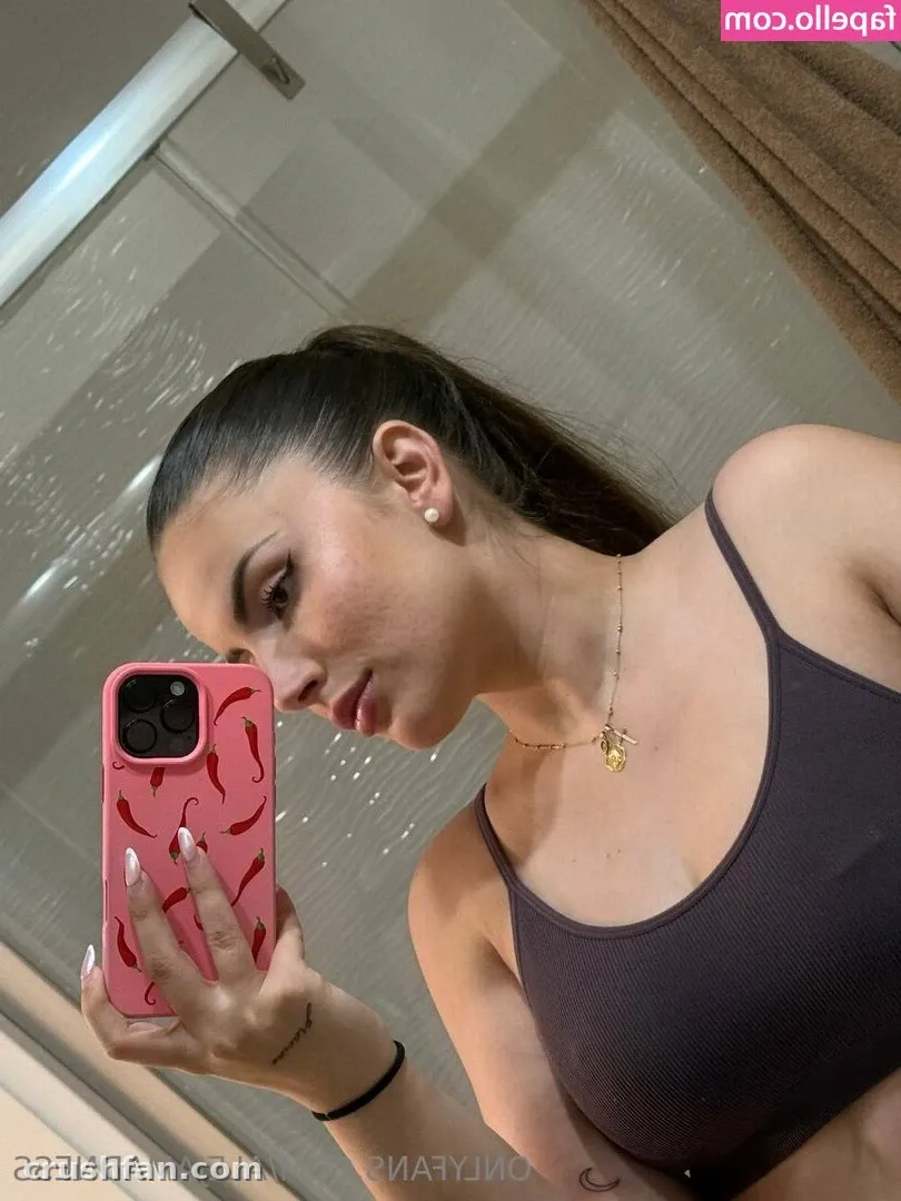 Creator in a dark tank top holding a pink chili-patterned phone in a mirror selfie.