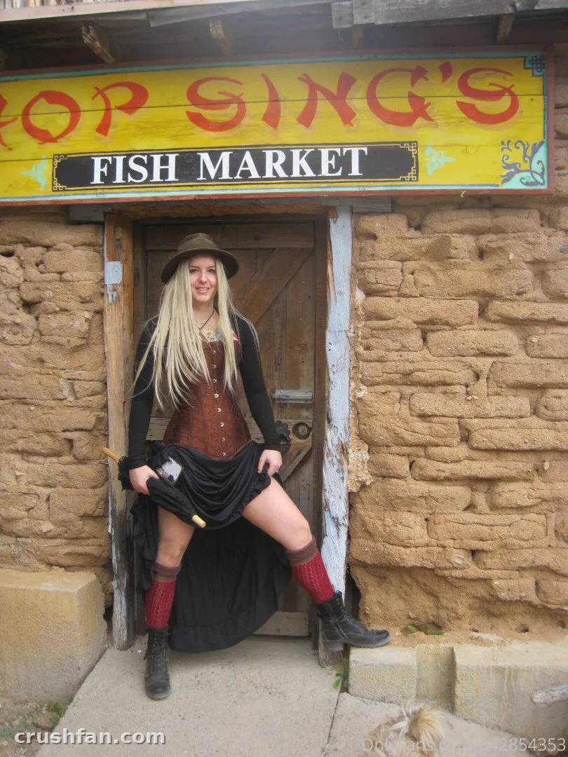 Kim in a wide-brimmed hat and dark skirt standing in a doorway beneath a yellow market sign