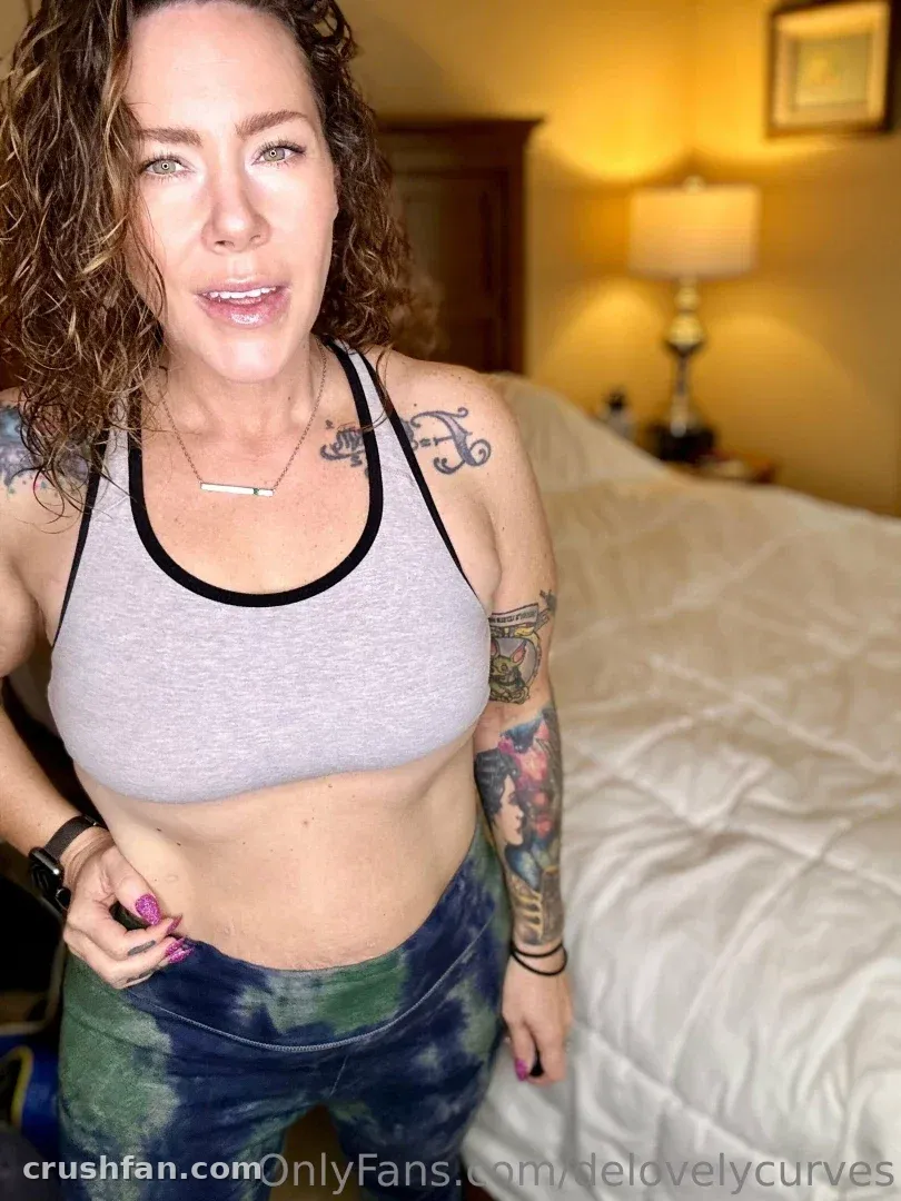 Creator in a grey sports bra and tie-dye leggings standing in a warmly lit bedroom.