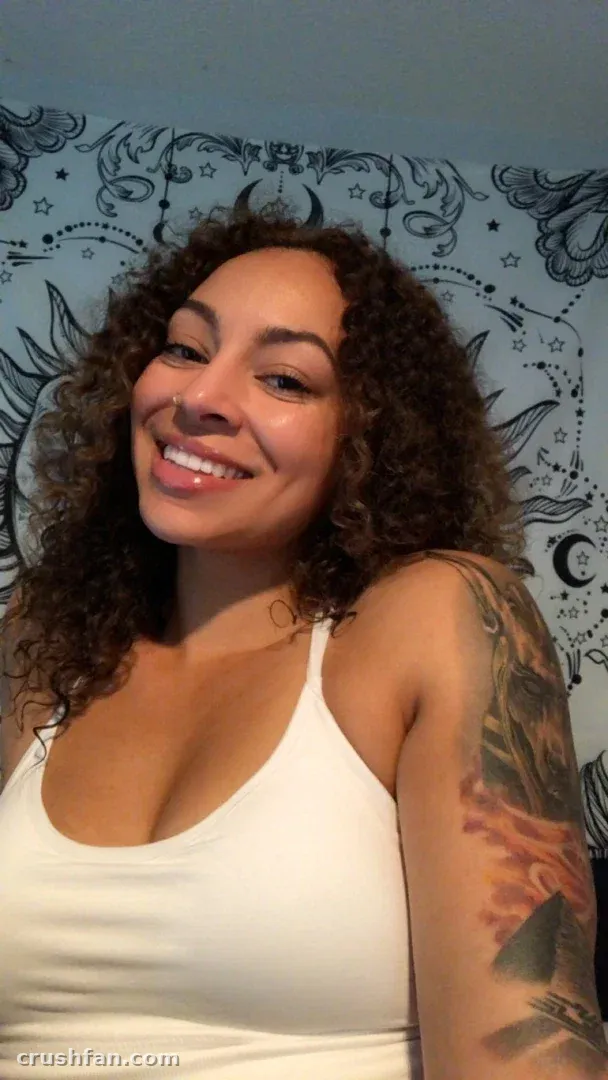 Leah in einem weißen Top lächelnd vor einer gemusterten Wand
