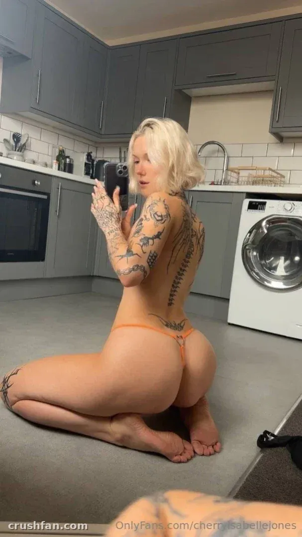 Cherry ajoelhada no chão da cozinha tirando uma selfie no espelho com uma tanga cor de pêssego