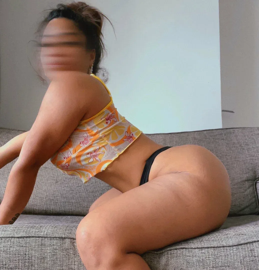 Creadora arrodillada en un sofá gris con un top corto amarillo de estampado cítrico en una habitación con luz suave.