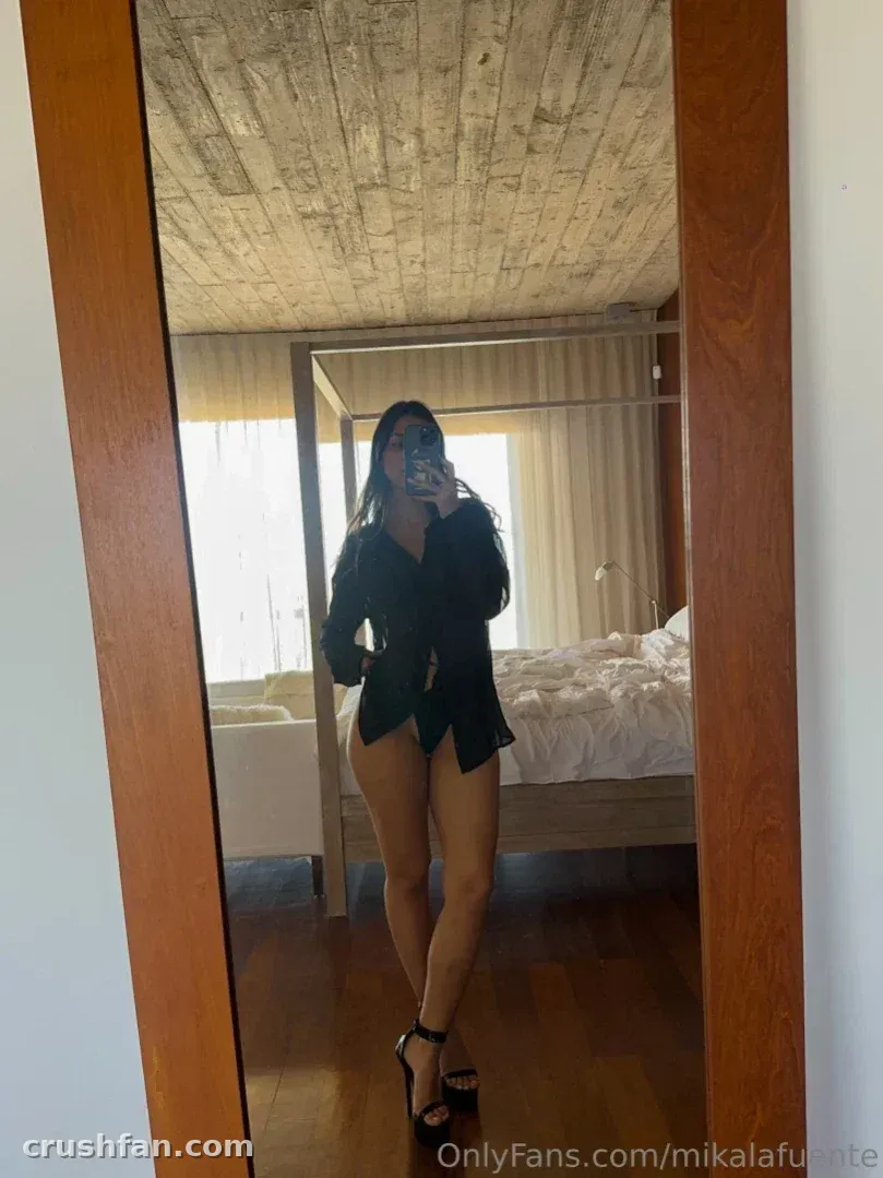 Mika in a black shirt dress taking a full-length mirror selfie in a bedroom