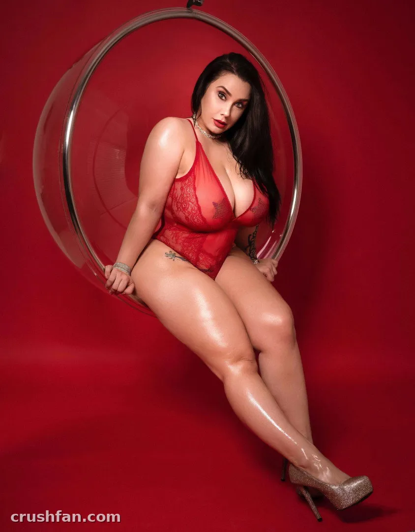 Romi Chase in red lingerie seated on a clear circular prop against a red background
