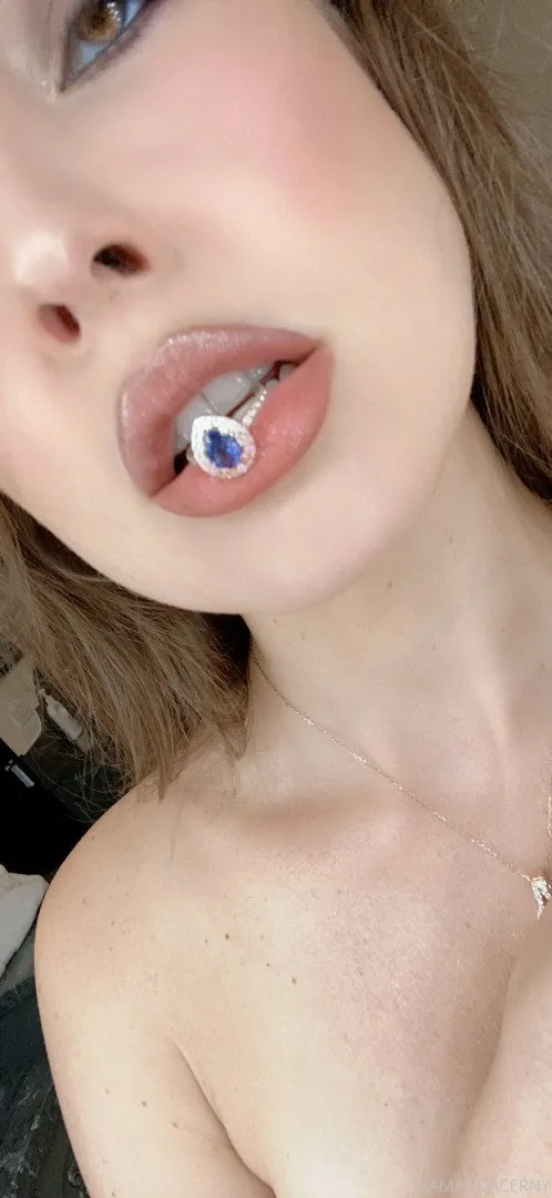 Крупный план Amanda Cerny, держащей кольцо с синим драгоценным камнем между губ.
