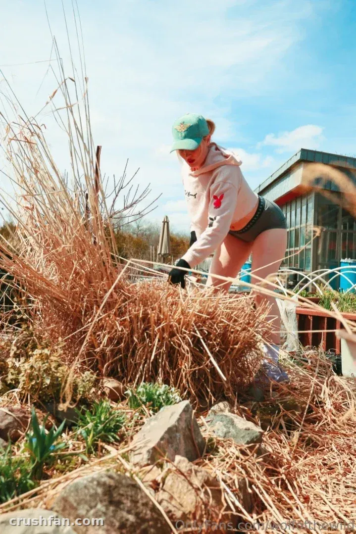 Holly Wolf in a pink hoodie and teal cap working in a sunlit garden bed